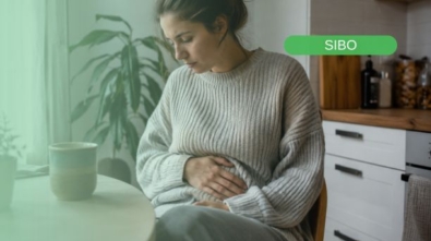 Mujer padeciendo uno de los síntomas más fracuentes del sibo: hinchazón abdominal y malestar digestivo